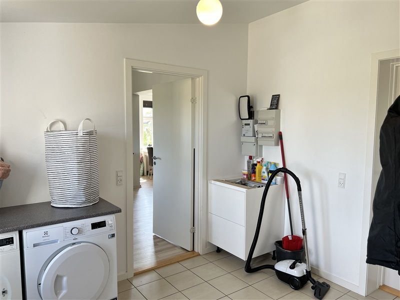 Renserirum med hvide vægge, gulv og apparater samt en lyseblå pose og en støvsuger med skovl