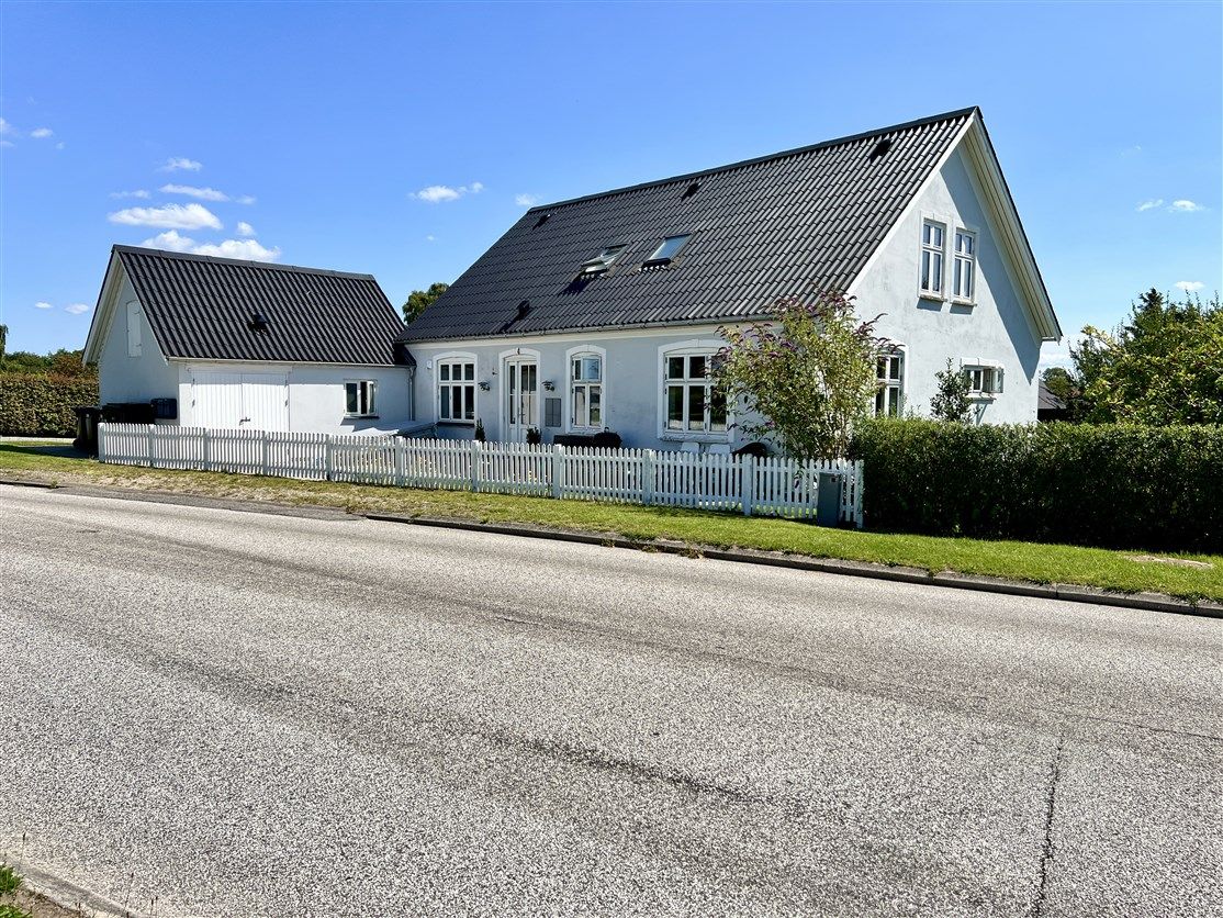 Hvidt hus med sort tag og hvide ruter, stående i Nørre Aaby, med terrasse og hvidt hegn