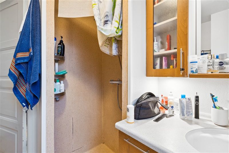 Bad med brusebad og en håndvask med flere kosmetiske produkter og en opbevaringsskab med indhold