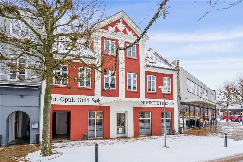 Oplysninger om optik- og guldforretning Munk Petersen i Ringe med snedækket og røde bygninger med hvide vinduerne