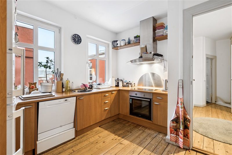 Lys, funktionel køkken med lyse lofter, lysegrå vægge, brædt gulv og hvide apparater