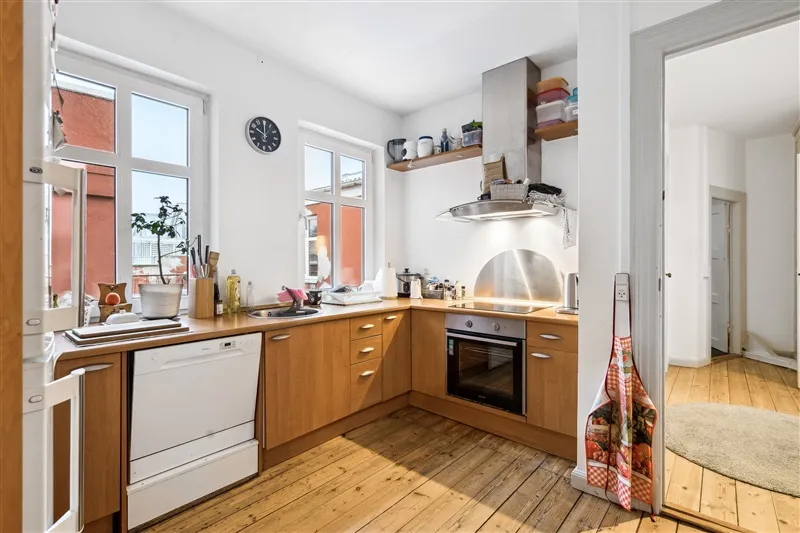 Lys, funktionel køkken med lyse lofter, lysegrå vægge, brædt gulv og hvide apparater