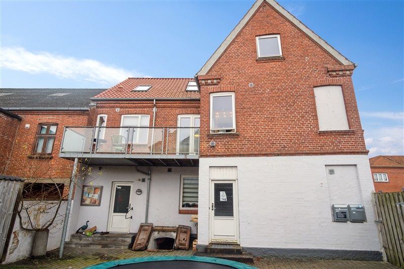 Rød og hvid stueetagen med 2 vinduer og balkon samt en trappe udenfor, der fører til første sal