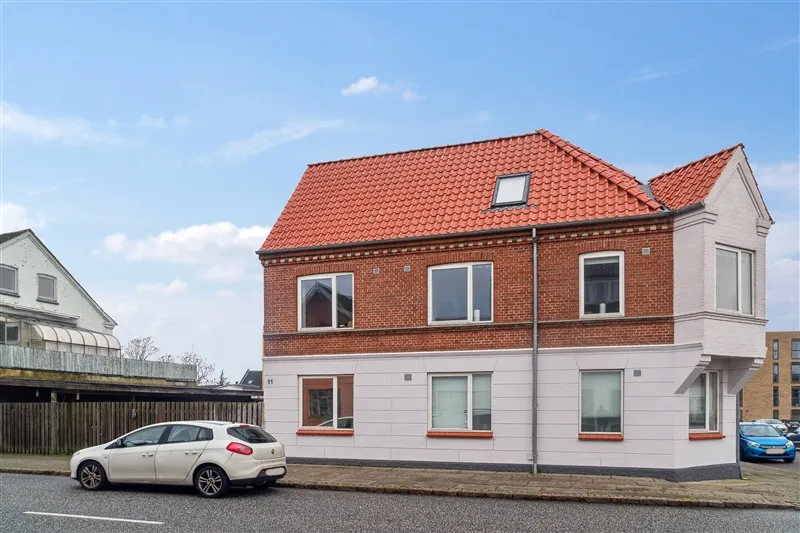 Sønderbrogade 11 i Tørring med smuk rødt tag og hvide vægge, to biler parkeret foran og en søjle mod gårdsplads