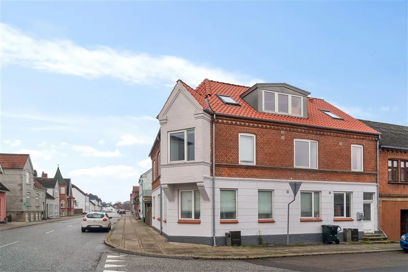 En bil kører langs Sønderbrogade, og der er en række bygninger med højde og røde tagdækninger i baggrunden.