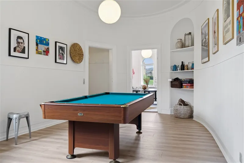 Poolbord med grønt felt står i lyse, moderne stue med hvidt panel og hylder med deko.