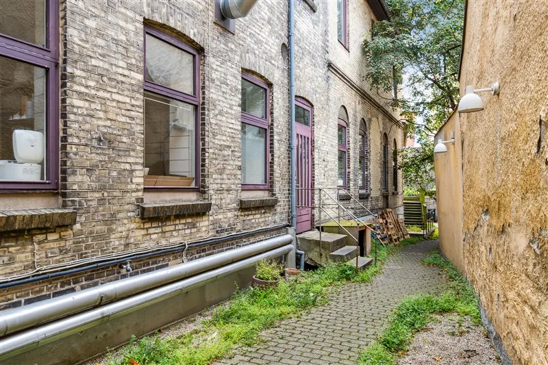 Bagside af en bygning i Svendborg med røde vinduer og lysegrå støbejernsrør langs facaden og skraverede vej med grønne