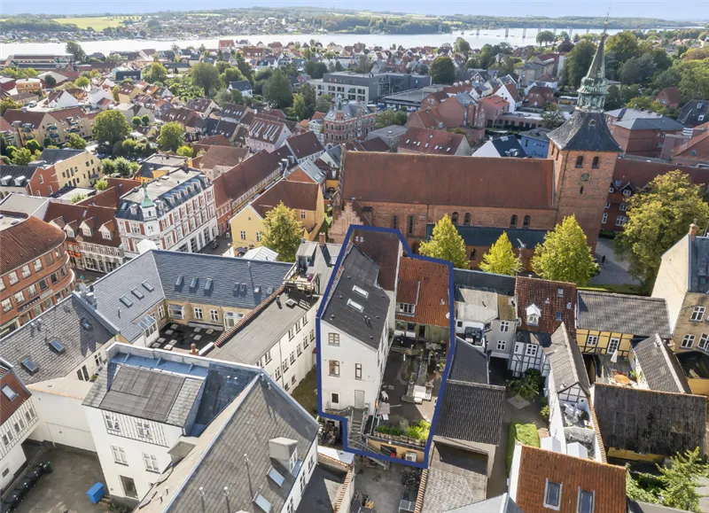 En oversigt af Svendborg by med mange huse og røde tag med en sø og bjerge i baggrunden