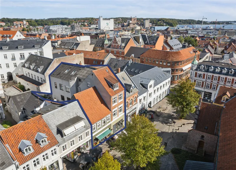 Kort over Svendborg med et moderne højhus i baggrunden, omgivende historiske bygninger med røde tag og grønne træer i