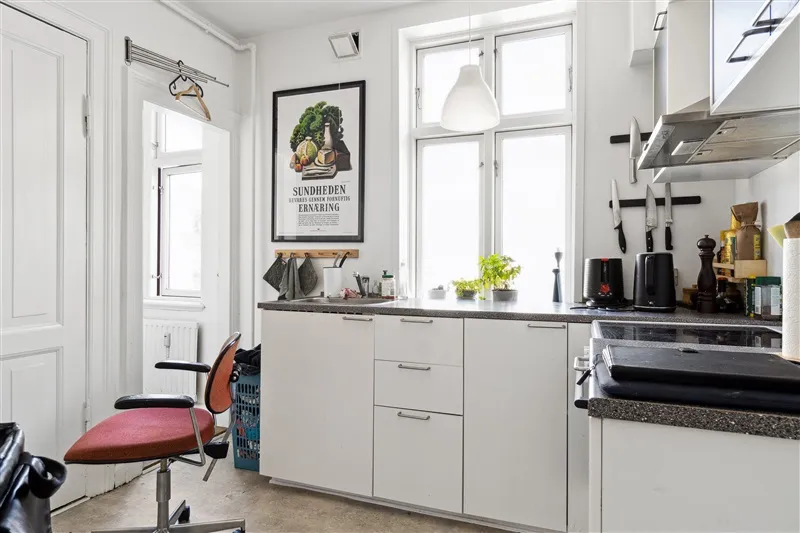 Minimalistisk køkken med hvide vægge og møbler, lysekroner, skarpe og pæne genstande og en skærm med tekst på væggen