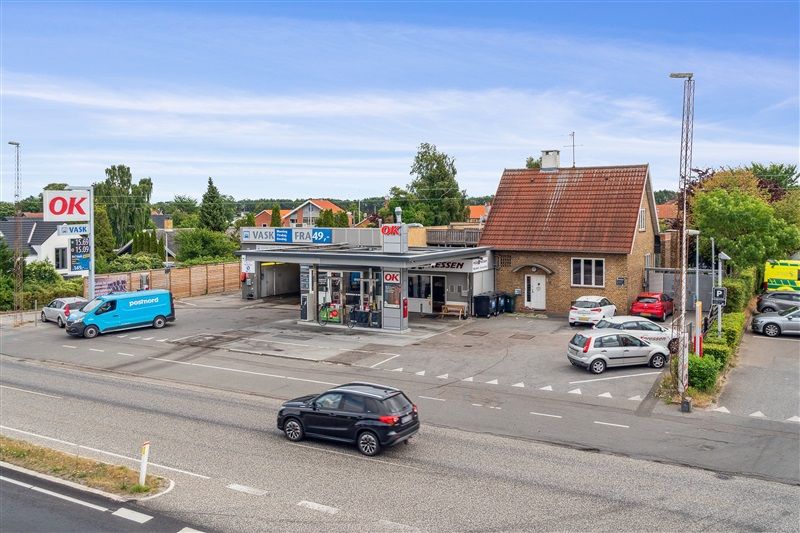 Udlejningsejendom med tankstation og kontorlokaler i Køge. Foran er flere biler parkeret og en kunde køber benzin.