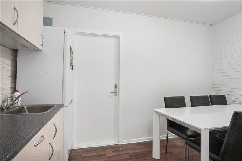 Et hvidt køkken med et køleskab, en ren hvid spiseplads med fire stole og en ren håndvask med vandhane