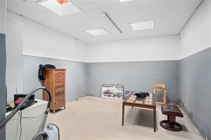 Et værelse med loftslampe og et skab med fire skuffer og en stol samt en skrivebord og en stol med lædersete