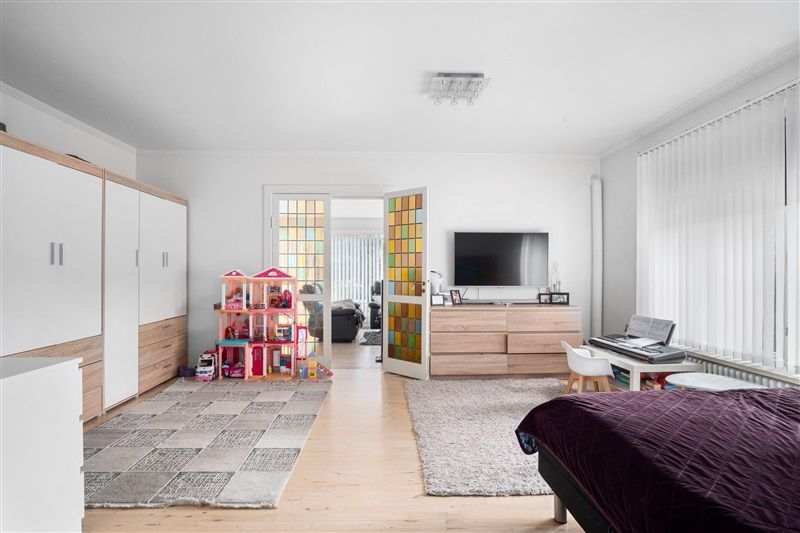 En moderne stue med lyse vægge, to gardiner, et tv, en klaver og en legetøjsvogn