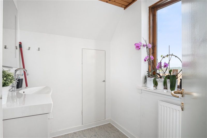 Rent og pænt badeværelse med hvidt badekar, hvidt vask og tre lyserøde orkideer i hvide potter på vindueskarm