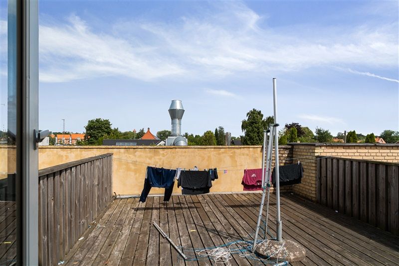 Loftsterrasse med tøjstativ og hængende tøj, udsigt over bygninger og træer på baggrunden