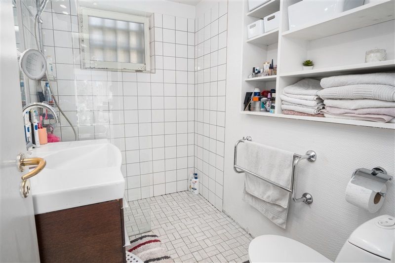 Et rent og velorganiseret badeværelse med hvide kakeloverflader og møbler, hvor der er en hvidt porcelænsbadekar og en hvidt