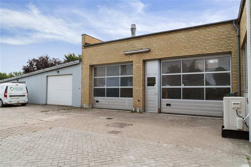 Vandkøler på bygning, garagedør, hvid varmepumpe, parkeringsplads, bus og røgaffugter på taget