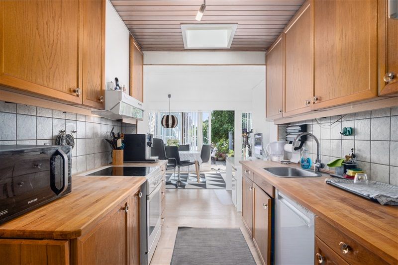 Foto af en moderne køkken med lysegrå vægge og træskabe, en ovn, komfur, vask, opvaskemaskine og mikroovn samt en bord og