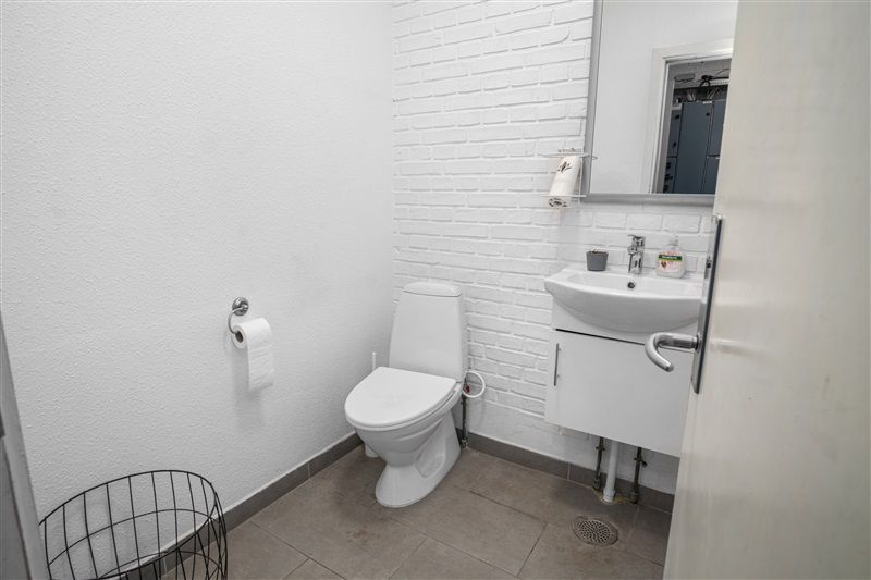 Et lille hvidt badeværelse med toilet, hvidt vask og håndvask samt spejl på væggen