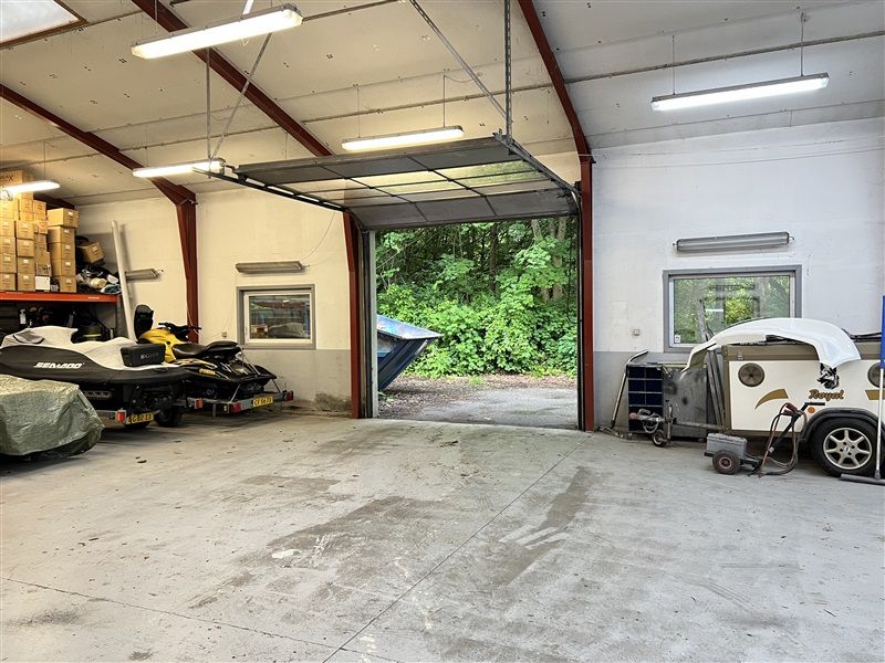 Et garage med åben garagedør og to skibe parkeret indenfor samt to bokse og lyskabler i loftet