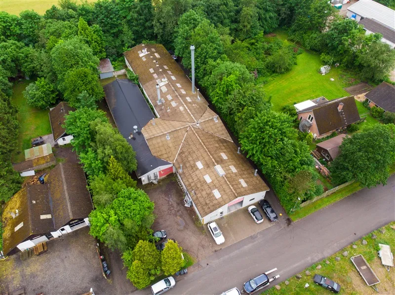 Bygninger og parkeringsplads i Them. Mange biler parkeret og området omgivet af grønne træer og buske.