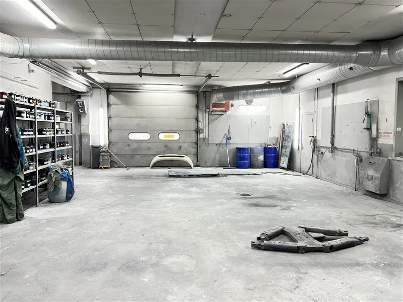 Ledig garage med rørgående ventilation, hængende værktøj og flere værktøjskuffer og skraldspande forskudt til siden