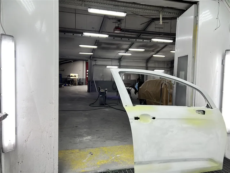 Bilport i produktionslokal med hvidt kabinet og lys i loftet samt gul gulv og mørk baggrund