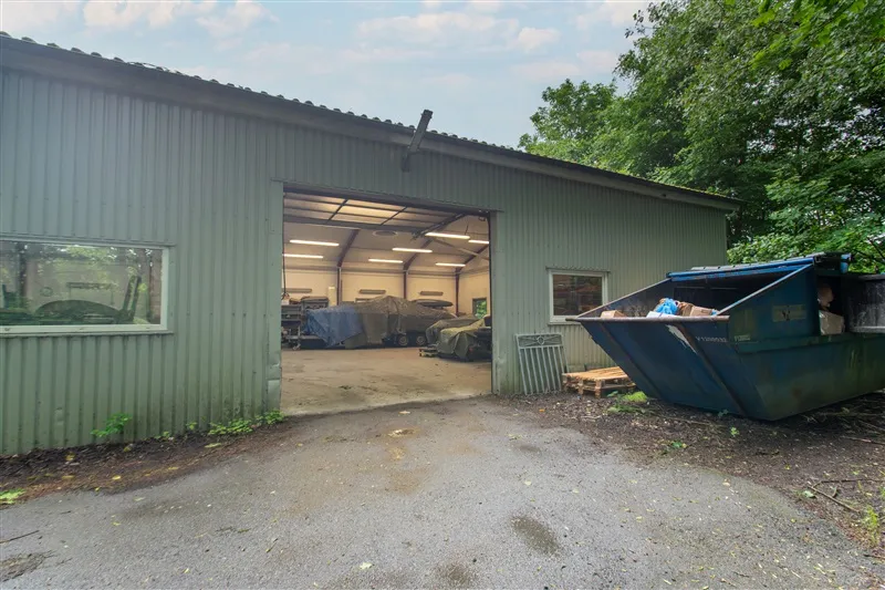 Lejerens garage i Knudlund med åbne døre og skraldspande udenfor. Værkstedet har flere biler og væsentlig grønt omkring.