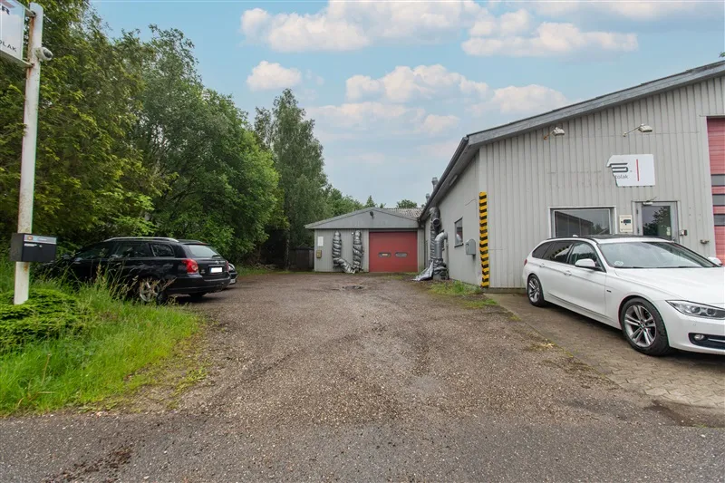 Erhvervsejendom med en stor parkeringsplads foran bygningen og en hvid BMW parkeret ved siden af