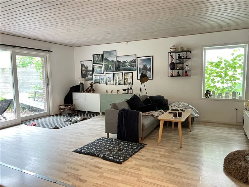 Moderne og komfortabel stue med lyse trægulve, gul sofa, træbord, kaffebord, hyggeligt indretning, kunstværker og store