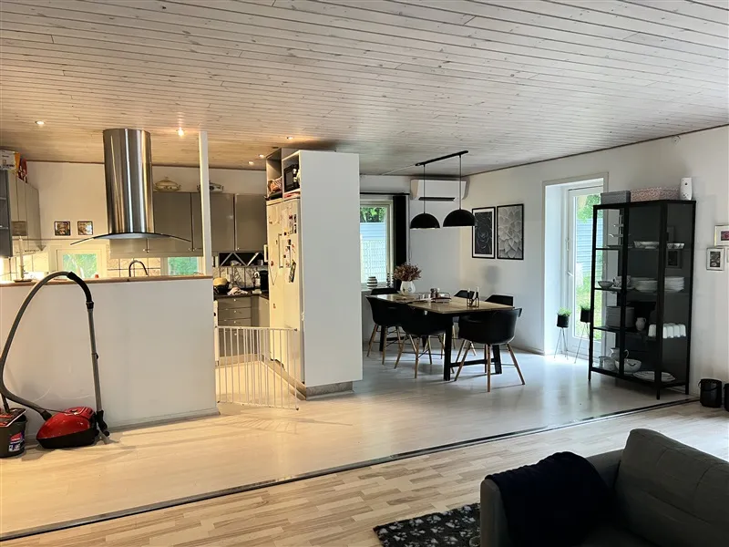 Et moderne køkken med lyse trægulve og hvide vægge, hvor der er en høj stående ovn og et køkkenbord med træben.