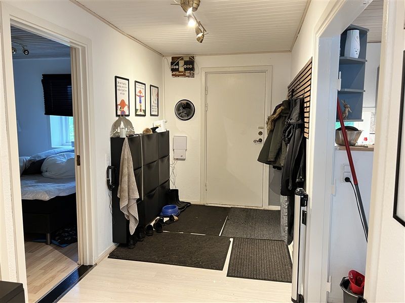 Foto af en hjørnegang med tøj og sko på gulvet og væggen og en seng med hovedpuder i rummet bag