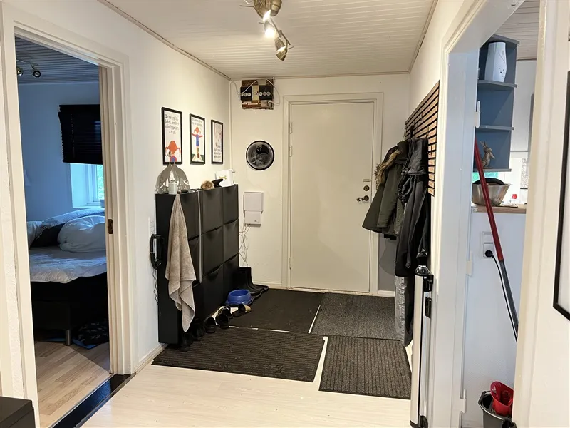 Foto af en hjørnegang med tøj og sko på gulvet og væggen og en seng med hovedpuder i rummet bag