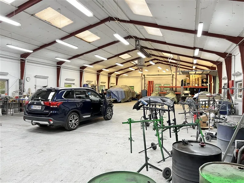 Erhvervslejemål med garage og værksted i Them. Der er en bilparkeret i garagen og andre bildele og værktøj i værkstedet.