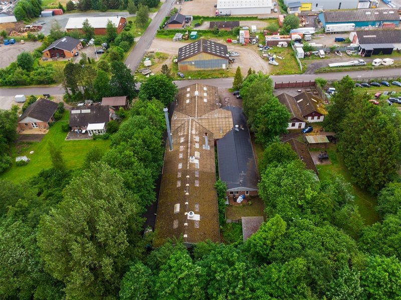 Et luftfoto over et industrikvarter med mange bygninger og parkeringspladser omgivet af grønne træer og buske