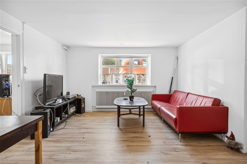 Moderne indretning med rødt lædersofa og trægulv, høj teknologi med flatscreen og lydanlæg og et vindue med udsigt til en