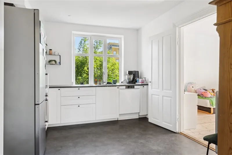 En moderne køkken med hvide vægge og loft, en stor vinduesfront og en stor køleskab samt en moderne ovn