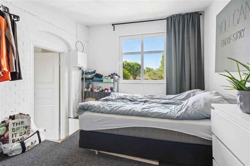 Hvidt soveværelse med enkeltseng og højre sidebord med plante og baggrundsvæg med skrift You can endofstory