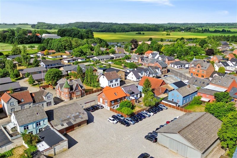 Forskellige bygninger med skrånende tag og flere parkerede biler i parkeringsområdet og en vej i et landsbyområde