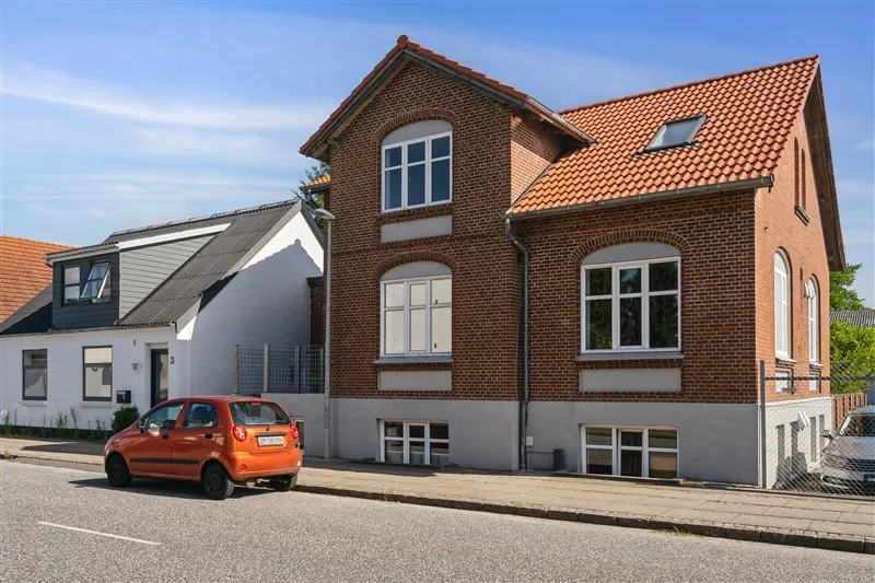 Udlejningsejendom på Sønderbrogade i Tørring med orange bil og to biler parkeret på siden