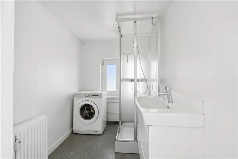 Et nyt, hvidt badeværelse med moderne radiator, en hvid tøjvask og et hvidt badekar med en bruser.