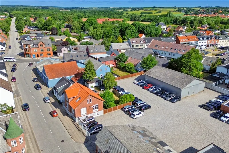 Forskellige farvede bygninger og mange parkerede biler og busser langs en gade i Tørring