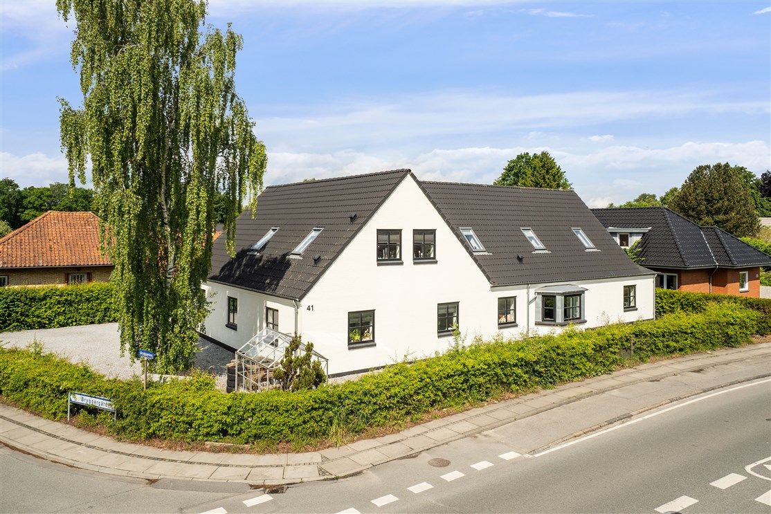 Huse i Otterup med smuk udsigt til grønne skove og blomstrende buske og træer under en blå himmel med skyer