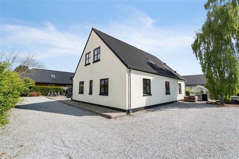 Hvidt renoveret hus med sort tag, fire vinduer, garage og flere brænde i baghaven