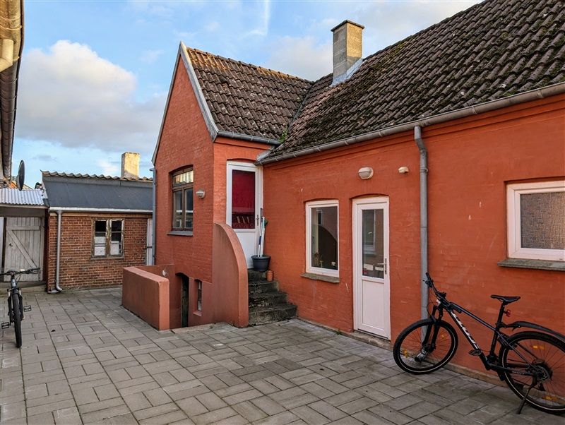 To cykler står parkeret foran en gammel murstenshus i Middelfart, hvor vinduer og døre er åbne