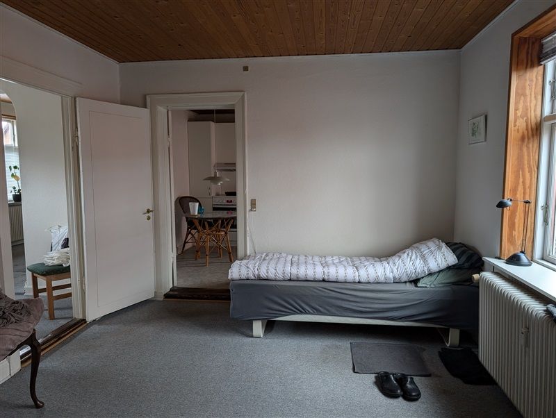 En lille værelse med hvidt loft og vægge, et enkelt seng med pude og dyne og en radiator på gulvet