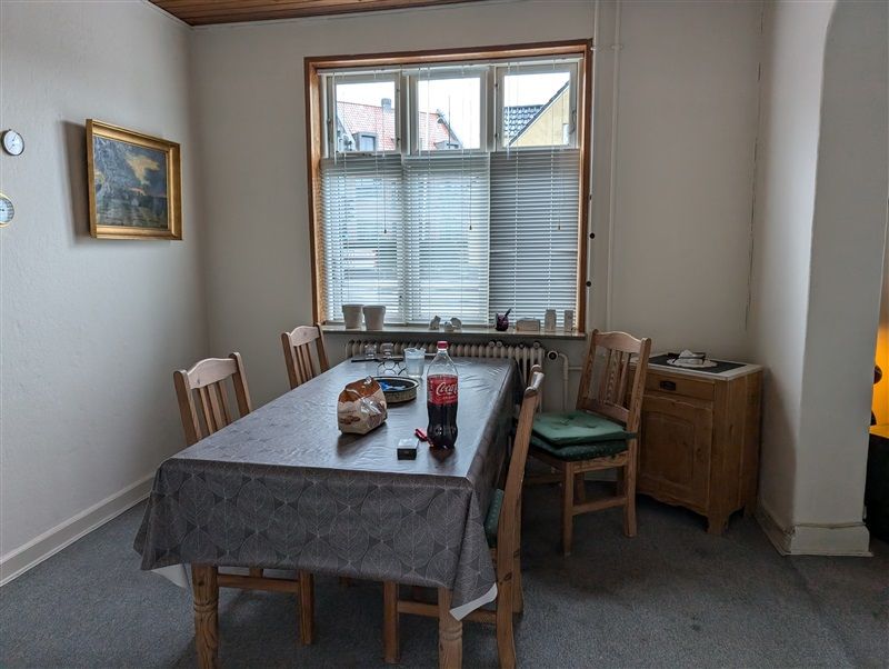 En spisebord med fire træstole og en Coca-Cola flaske på bordet og et spil briller i en række.