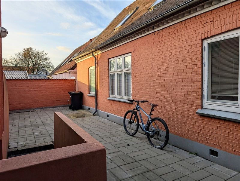 En cykel står parkeret ved en terrasse på en bygning med røde mursten og hvide vinduer i Middelfart