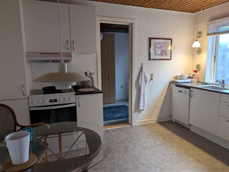 Nydelig køkken med moderne hvide skabe og bord, hvor der står en hvid plastkrus og en glasbord